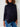 Person wearing a black turtleneck sweater and blue jeans against a white brick wall.