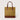 A structured tote bag with a textured mustard-yellow body, brown leather handles, and a brown leather base, shown against a light gray background.
