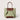 A structured tote bag in light sage green canvas with contrasting brown leather trim, double top handles, and a matching brown base panel, shown against a solid light beige background.