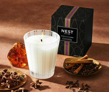 Nest Moroccan Amber Collection Candle - this image features the candle and the package in which it comes surrounded by amber, cinnamon, star anice and cloves.