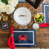 Dining table setting with a crab-themed place mat, white flowers, and appetizers.
