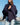 Woman wearing a dark blue poncho by a waterfront with boats in the background