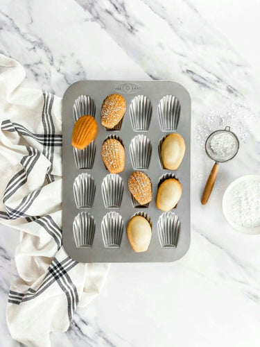 Metal madeline tin with baked goods on a marble surface