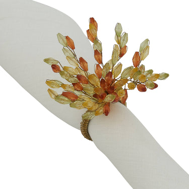 A gold-toned napkin ring bracelet  clustered translucent amber, orange, and pale yellow leaf-shaped beads, shown worn on a white fabric napkin.