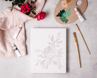 Floral design on paper with art supplies including paint, brushes, and flowers.
