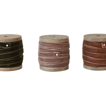 Three wooden spools wrapped with velvet ribbon. One has an olive green ribbon secured with a pin, one has a fawn colored ribbon secured with a pin, and one is a burnt orange colored ribbon secured with a pin.