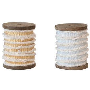 Two Wooden spools one with gold and one with silver metallic ribbon, both ribbons have a cotton fringe edge