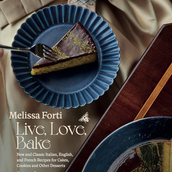 Cover features a woman in a black top, and a taupe colored satin skirt holding a blue ruffled edge plate with a chocolate iced piece of cake. She is holding a fork in her right hand. On the dark wood table in front of her is a platter with the rest of the cake with her slice taken out.