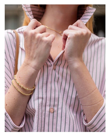 Person wearing a gold bracelet and gold necklace with a striped shirt.