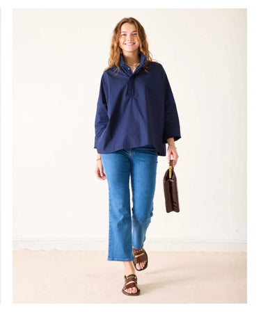 Woman wearing a navy blue top and blue jeans, holding a brown bag on a white background