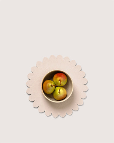 Three small pears in a small beige bowl placed on a scalloped beige placemat against a light warm gray background.
