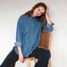 Woman wearing a chambray button down top sitting on a leather chair
