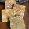The Painted Lily - Golden Tapestry stone coasters. Each one has a different tapestry design. Grey/sepia tone and white print over a golden yellow background.